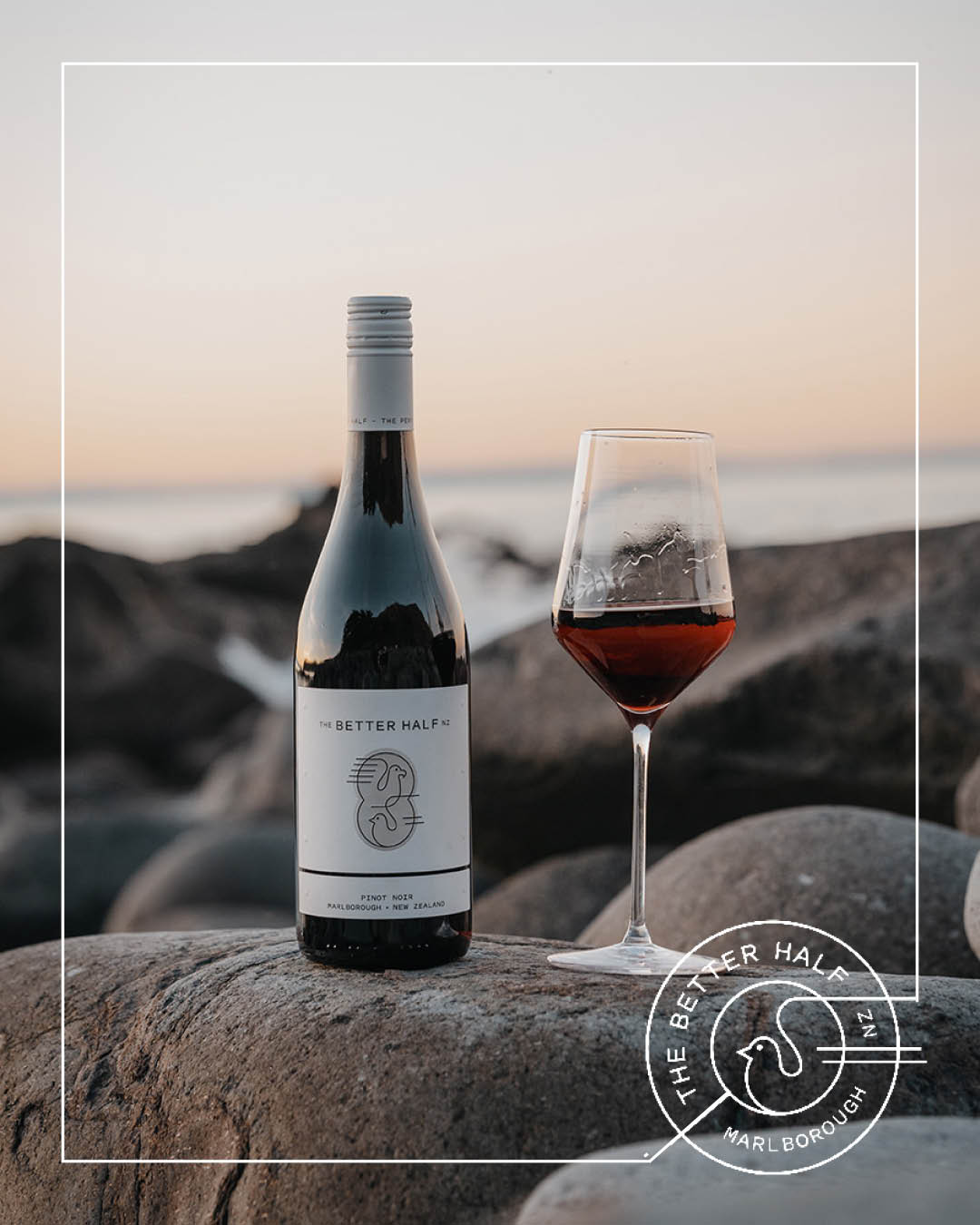 TBH Social 63 Bottle of The Better Half Pinot Noir with a glass of wine on rocks by the sea